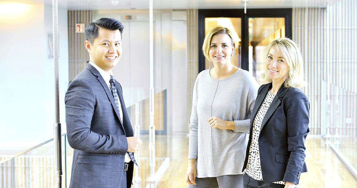 Three colleagues turn and smile in a modern office corridor